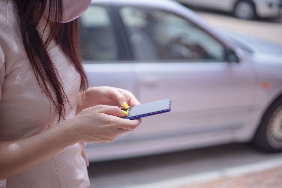 駐車している車の近くでスマートフォンでメッセージを送っている女性のクローズアップ。