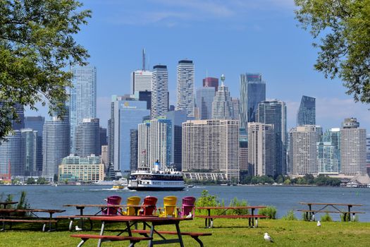 Vibrant view of Toronto skyline with waterfront, ferry, and colorful chairs on a sunny day.