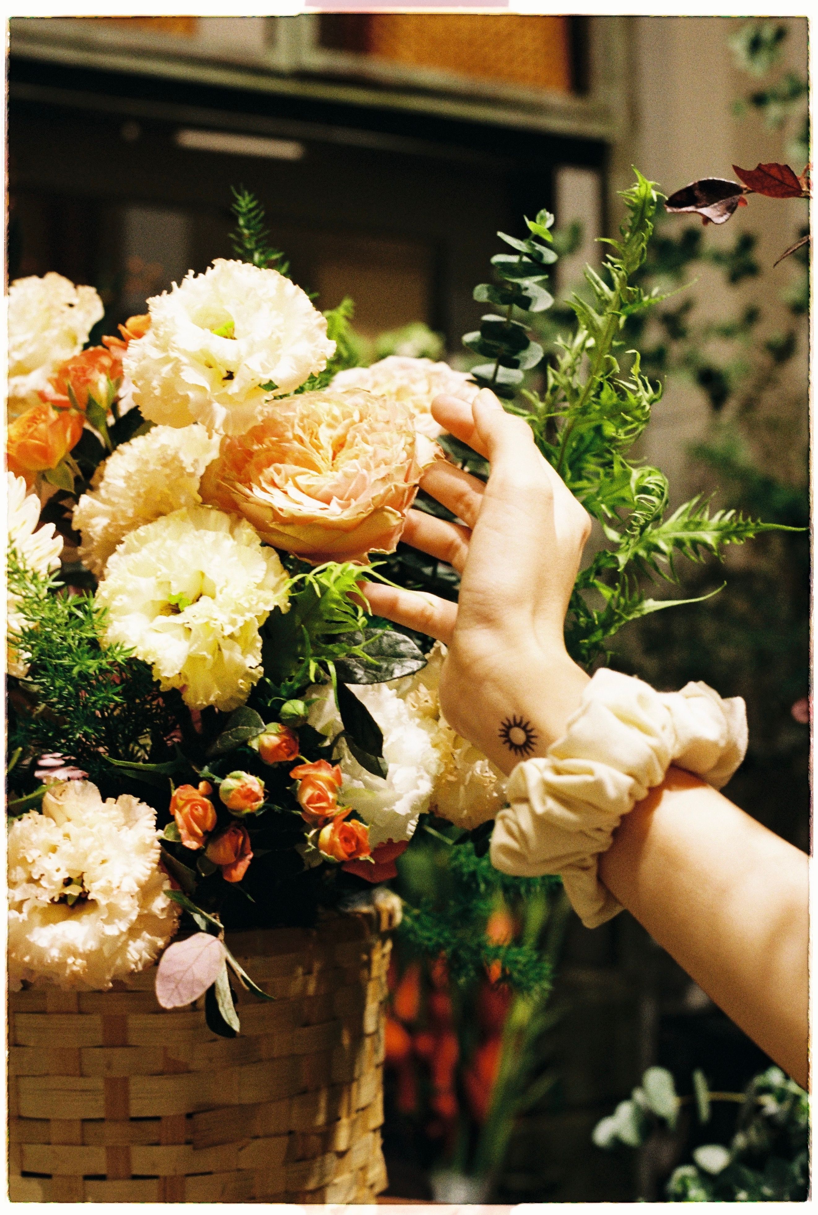 Hand reaching for a blooming flower in an artistic floral arrangement.