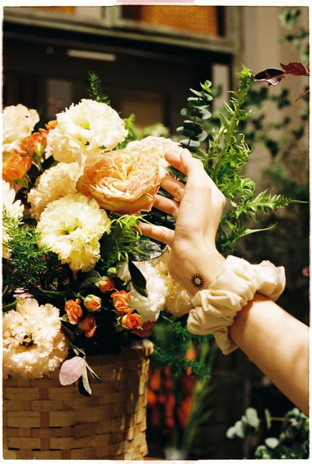 Hand reaching for a blooming flower in an artistic floral arrangement.