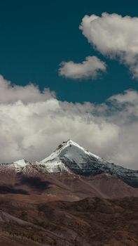 Beautiful view of a snow-capped mountain peak surrounded by clouds and a clear blue sky.