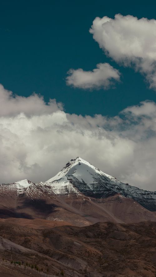 Free Beautiful view of a snow-capped mountain peak surrounded by clouds and a clear blue sky. Stock Photo
