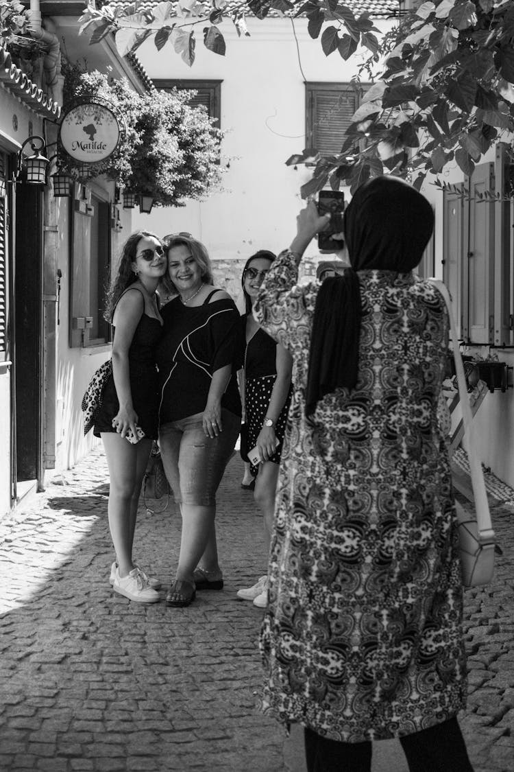 
A Grayscale Of A Woman In A Hijab Taking A Picture Of A Group Of Women