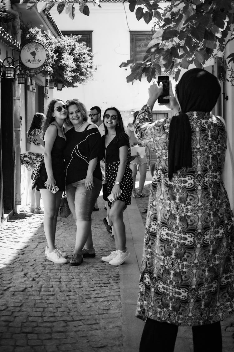 
A Grayscale Of A Woman In A Hijab Taking A Picture Of A Group Of Women