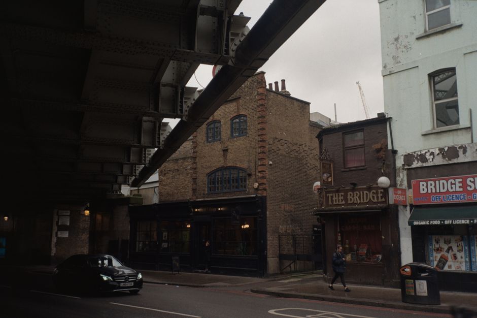 Street under bridge in London with historic buildings and a car passing by.