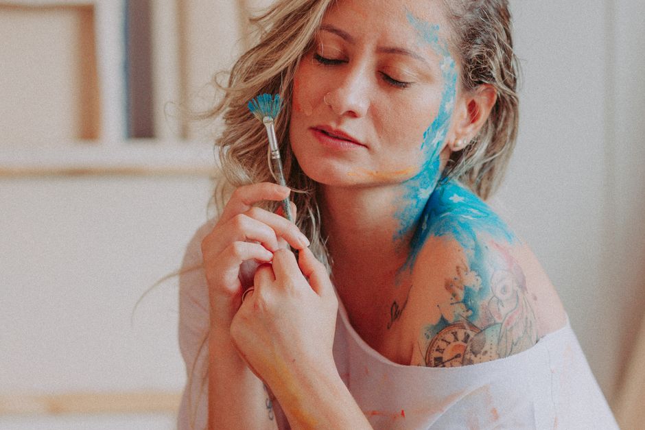Como a Criatividade Pode Aumentar sua Autoestima Diária 2 An artistic portrait of a woman with face and body paint holding a brush, eyes closed.