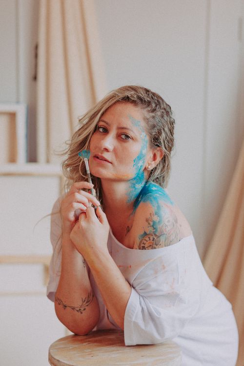 Free A portrait of a woman with tattoos holding a paintbrush, featuring blue paint on her skin. Stock Photo