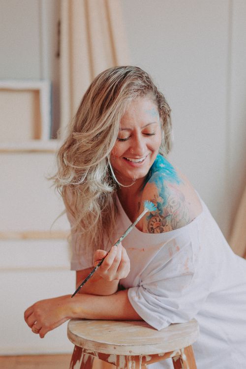 Free An adult woman smiling while applying blue paint on her shoulder with a brush. Stock Photo