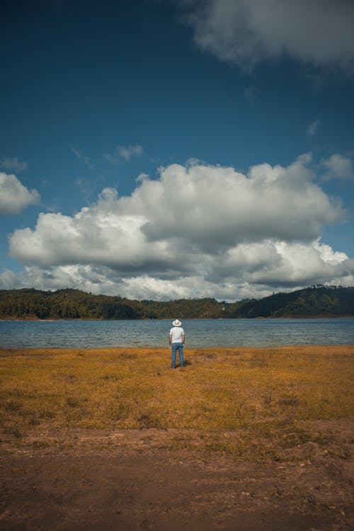 A Man in a White Shirt and Denim Pants Looking at a Lake