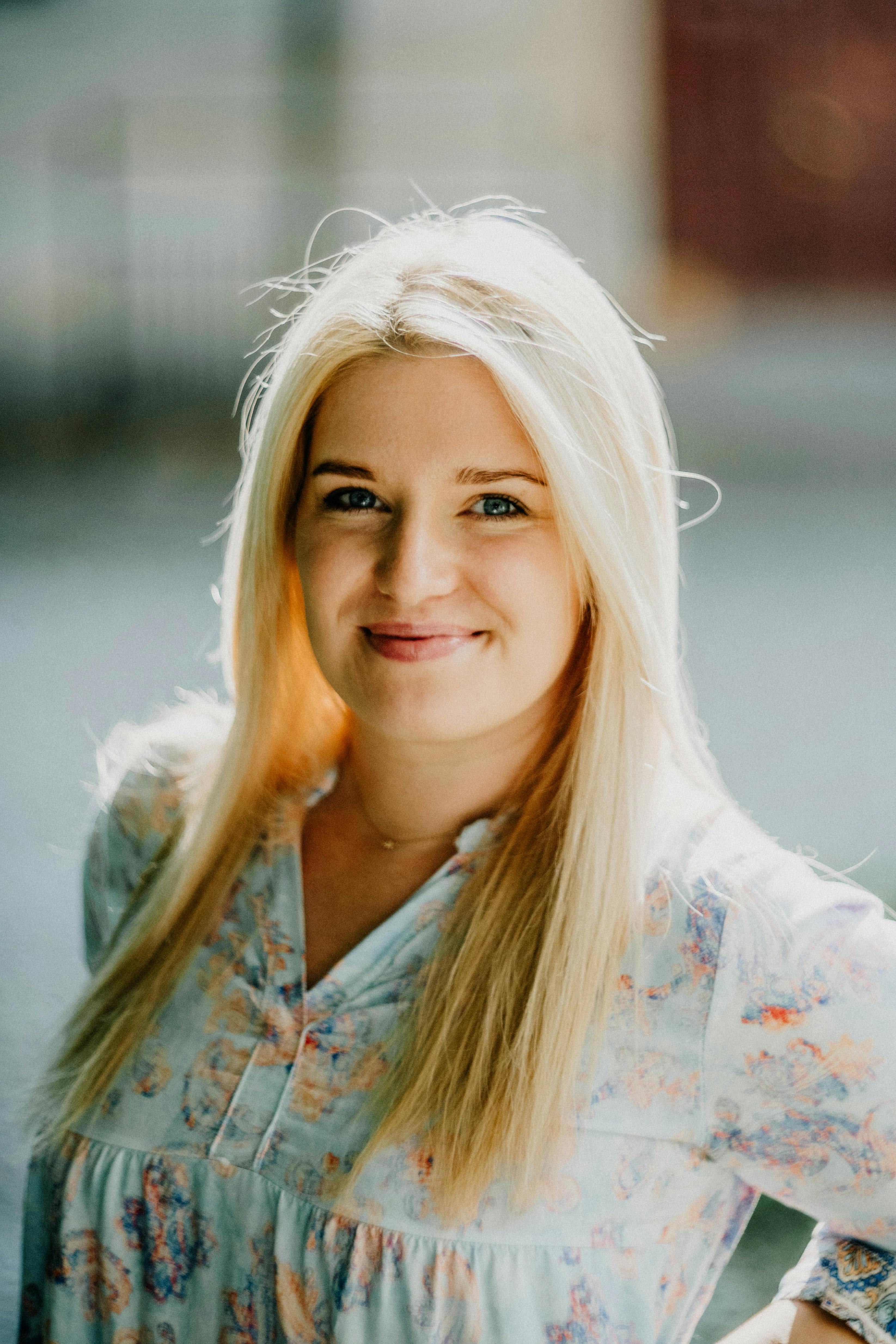 Portrait of a smiling young woman with long blonde hair in an outdoor setting.