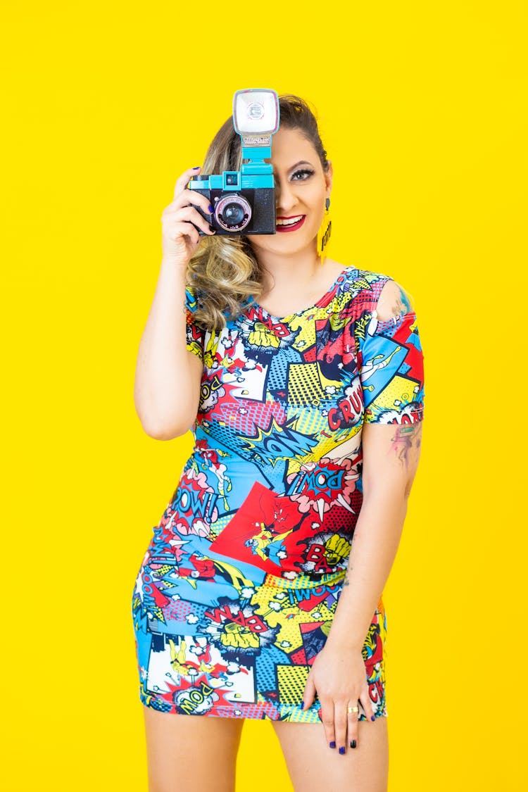 A Woman In A Comic Designed Dress Taking A Picture With A Camera
