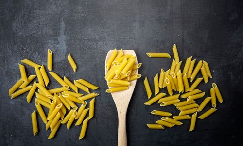 Free Top view of uncooked penne pasta and wooden spoon on a black surface, perfect for food-related content. Stock Photo