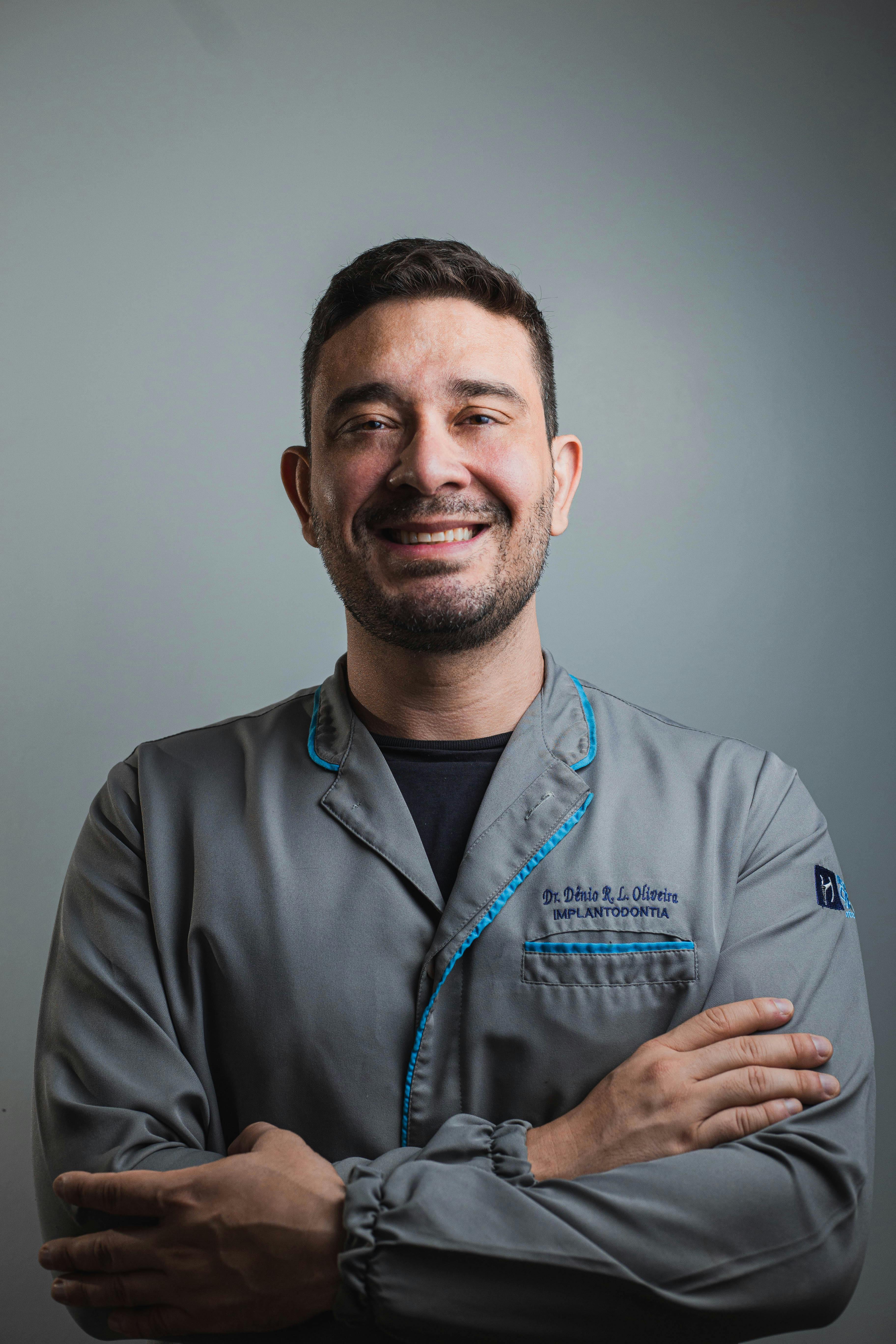 Smiling man in a scrub suit, arms crossed, against a neutral background.