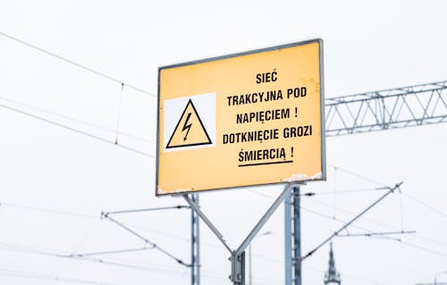 A Yellow Warning Sign Near High Voltage Steel Poles
