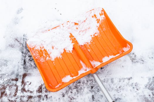 Close-up of an orange shovel on snow, depicting winter snow clearing.