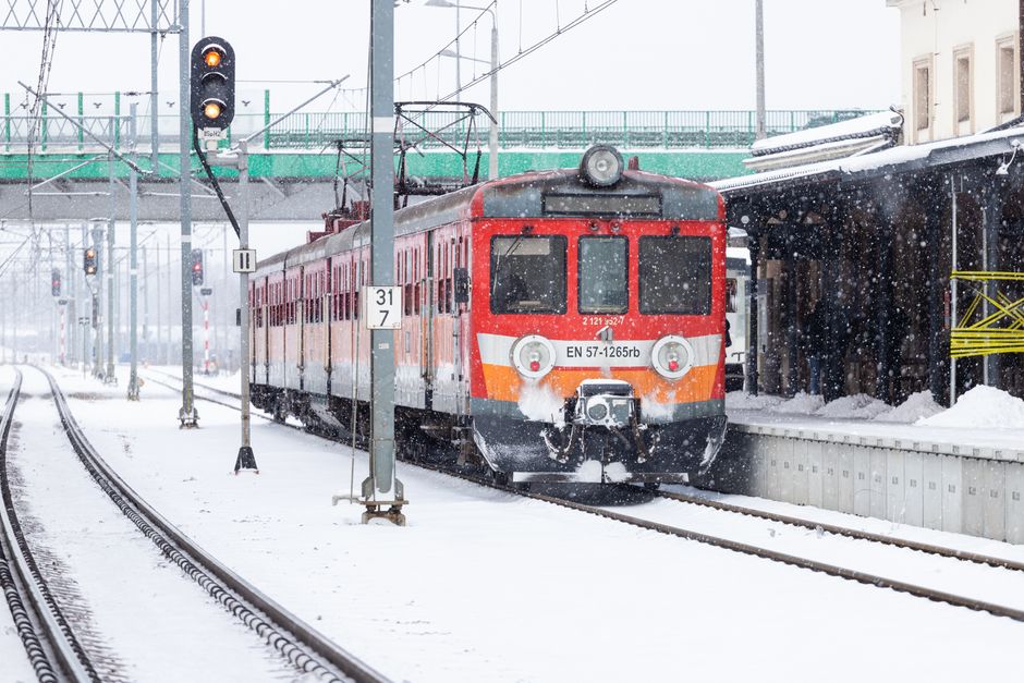A red train arrives at a snowy winter railway platform under falling snowflakes.
