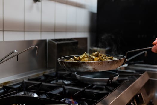 Sizzling mushrooms being sautéed in a pan in a professional kitchen setting, highlighting culinary preparation.