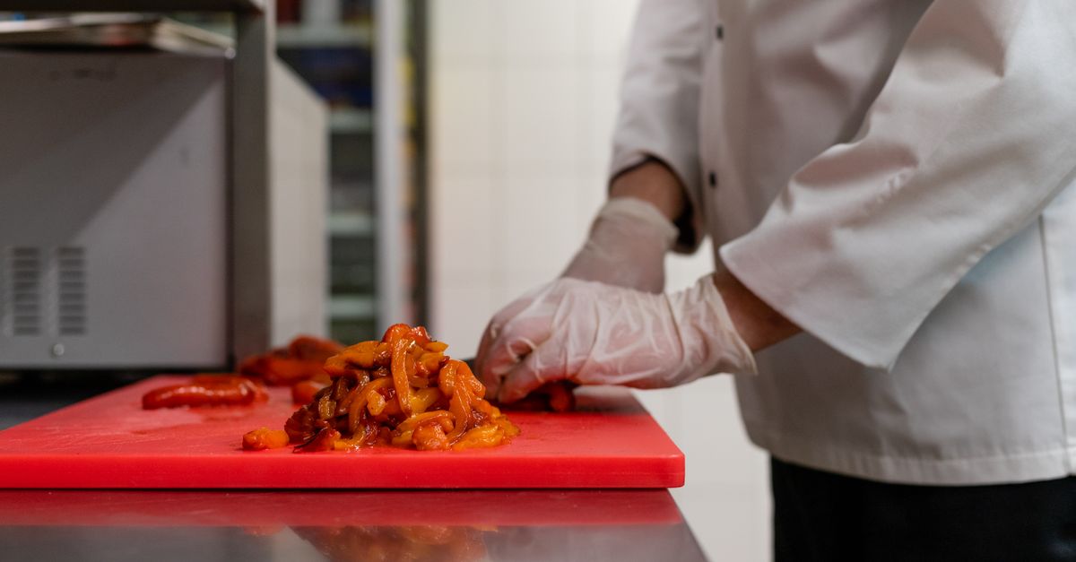 Photo by Mateusz Feliksik Chef chopping vegetables on a red cutting board in a professional kitchen.