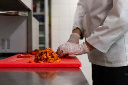 Chef chopping vegetables on a red cutting board in a professional kitchen.