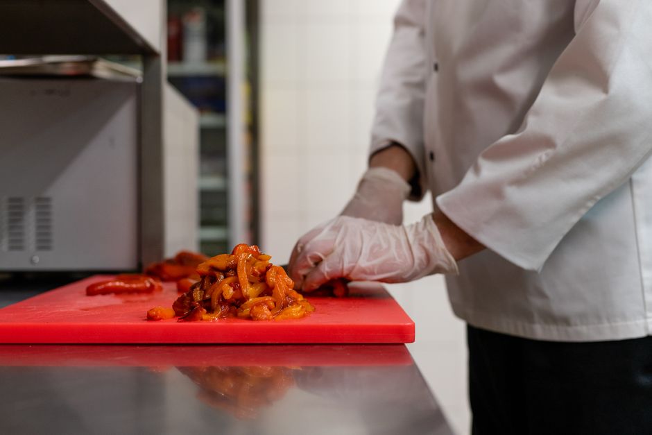 Chef chopping vegetables on a red cutting board in a professional kitchen.