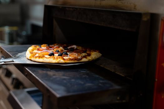 Close-up of a delicious pizza with various toppings being baked in an oven on a pizza paddle.