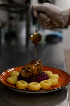 Chef pouring sauce over gourmet meal in professional kitchen setting.