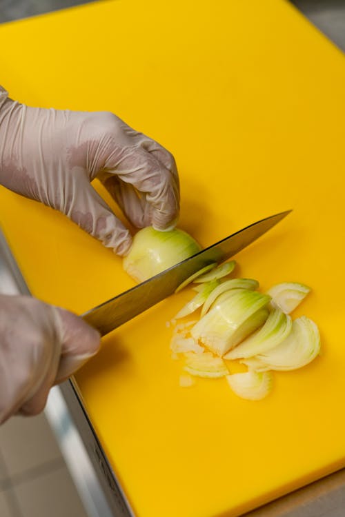 Free Close-up of gloved hands slicing onions on a yellow cutting board. Stock Photo