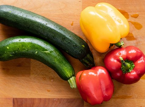 A vibrant display of bell peppers and zucchinis on a wooden surface, showcasing their freshness.