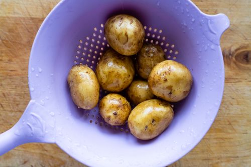 Free Top-down view of wet potatoes in a purple strainer on a wooden surface. Stock Photo