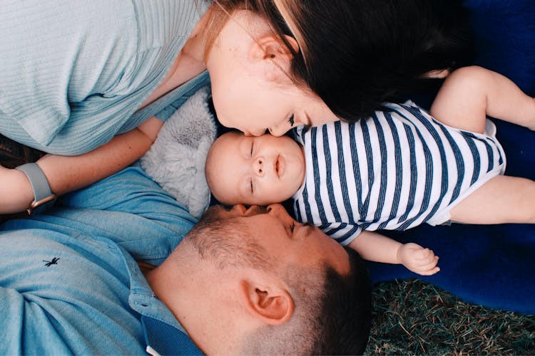 Couple Lying And Kissing Baby Lying Between Them 