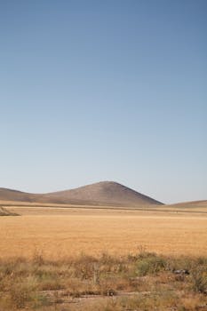 Tranquil view of Turkish countryside with a gentle mountain under a clear sky, showcasing nature's beauty.