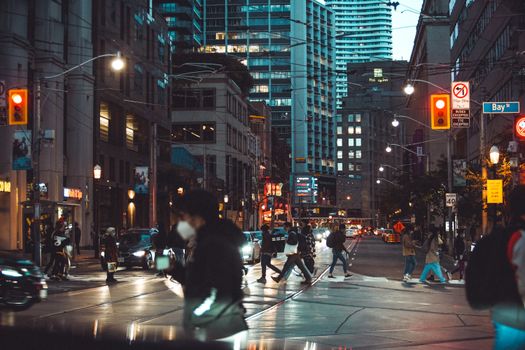 Dynamic city street at night with people crossing and towering buildings in downtown Toronto.