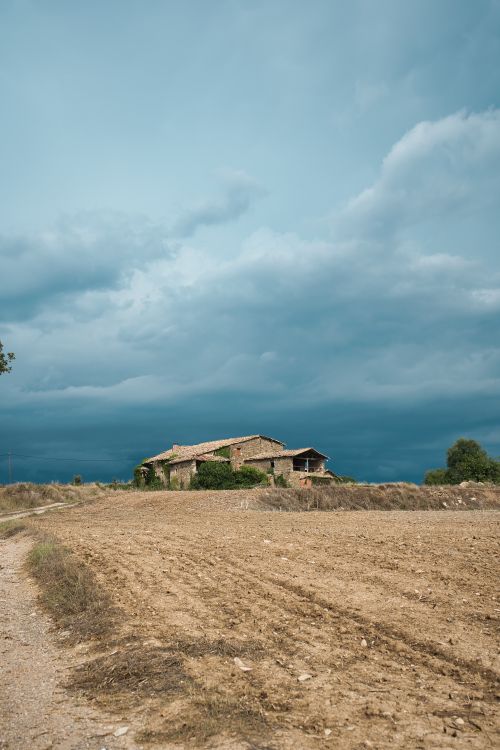 Free A serene view of an abandoned house surrounded by an open field under a blue sky. Stock Photo