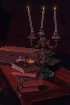 A vintage setting featuring lit candlesticks and antique books on a wooden table.