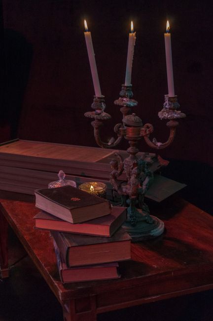 A vintage setting featuring lit candlesticks and antique books on a wooden table.