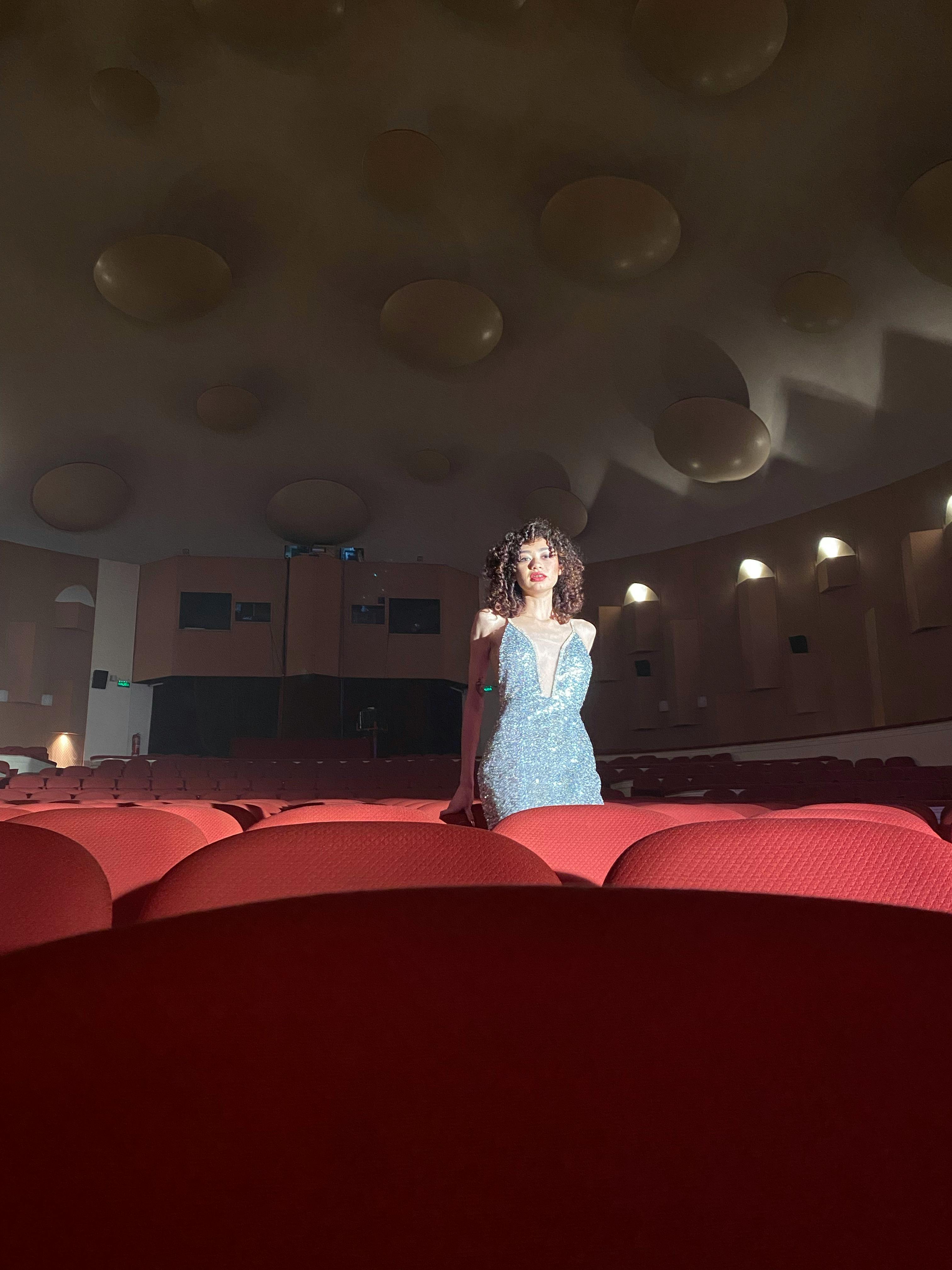 Free Glamorous woman in a sparkling dress standing gracefully in empty theater. Stock Photo