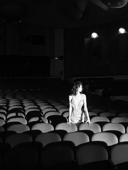 Woman standing among theater chairs in black and white lighting.