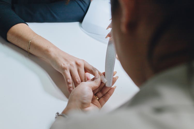 A Manicurist Filing A Client's Nail