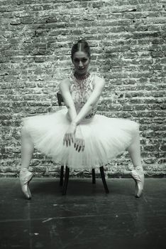Graceful ballerina in a classic tutu poses elegantly against a rustic brick wall.