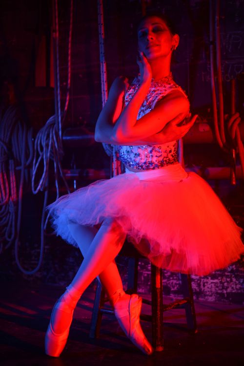Free A ballerina poses gracefully while seated, illuminated by vibrant red lighting. Stock Photo