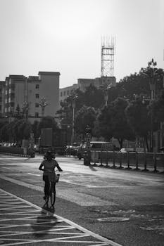 A cyclist rides through an urban street, silhouetted by morning light.
