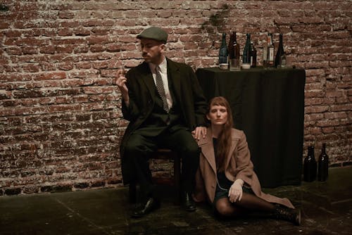 Man in Black Suit Sitting Beside a Woman in Brown Coat