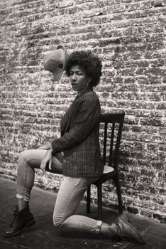 Black and white portrait of an afro-haired woman posing fashionably against a textured wall.