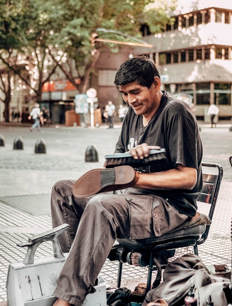 A Man In A Black Shirt Shining A Shoe