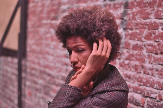 A thoughtful woman with afro hair poses against a textured brick wall.