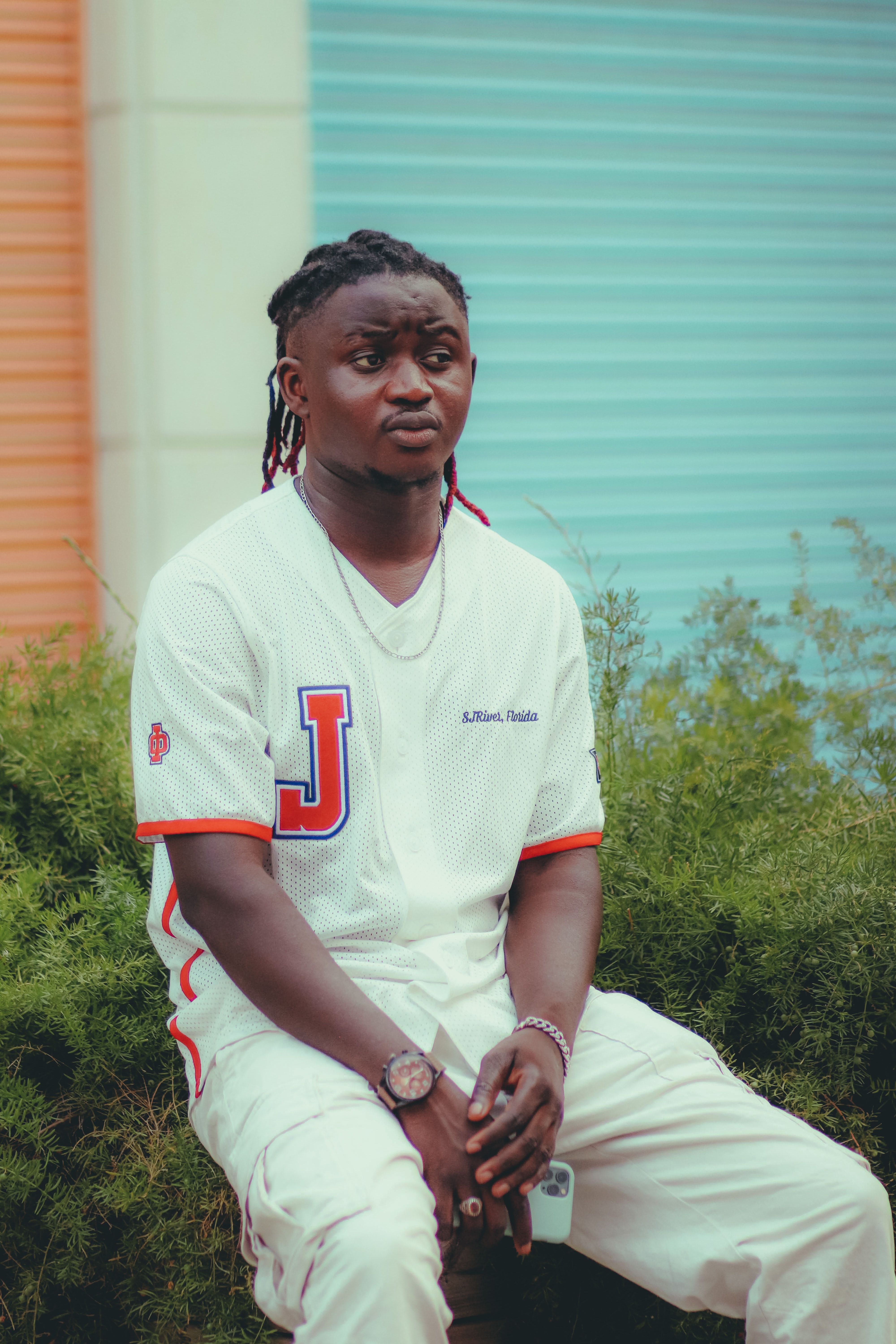 Fashionable young man with braids wearing stylish urban outfit in front of colorful background.