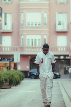 A man walks casually down a city street, embodying modern urban style in a white sports jersey.