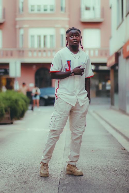 Free Full-body shot of a stylish young man in casual streetwear standing confidently in an urban environment. Stock Photo