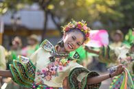 A smiling woman in vibrant traditional attire performs at a cultural festival, exuding joy.