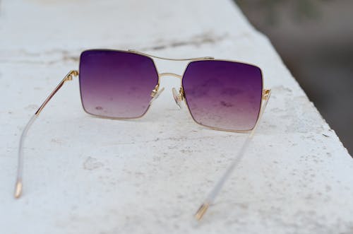 Gratis Gafas De Sol Con Lentes Moradas Enmarcadas En Color Dorado Sobre Una Superficie Gris Foto de stock